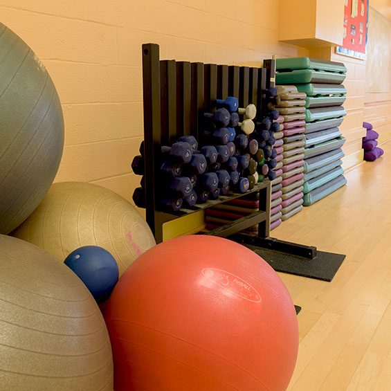 Several exercise balls are stacked in a corner next to a rack of a variety of hand weights in one of our multipurpose rooms in the Sullivan Recreation and Fitness Complex on our Portland campus. Stacks of fitness step platforms are in the background.