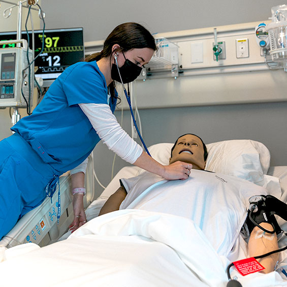 A nursing student checks the vital signs of a simulation lab dummy.