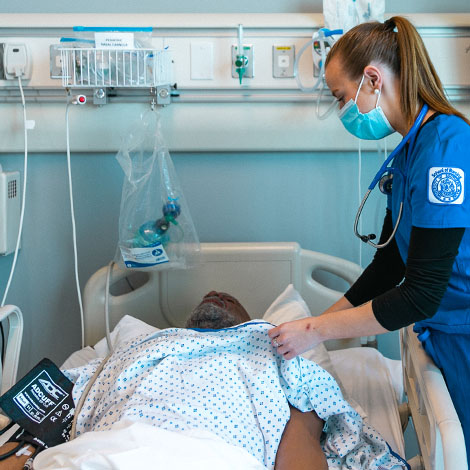 A student wearing School of Nursing scrubs checks on a mannequin patient in our simulation lab.