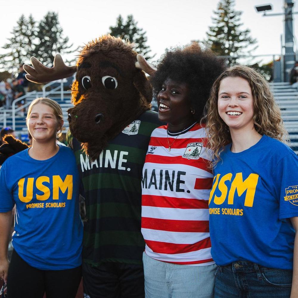 Three USM Promise Scholars pose with the Hearts of Pine moose mascot.