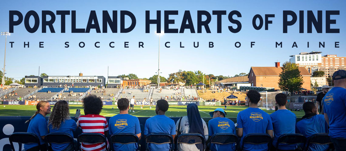 USM students watching a Hearts of Pine game. The words "Portland Hearts of Pine, the Soccer Club of Maine" are above their heads.