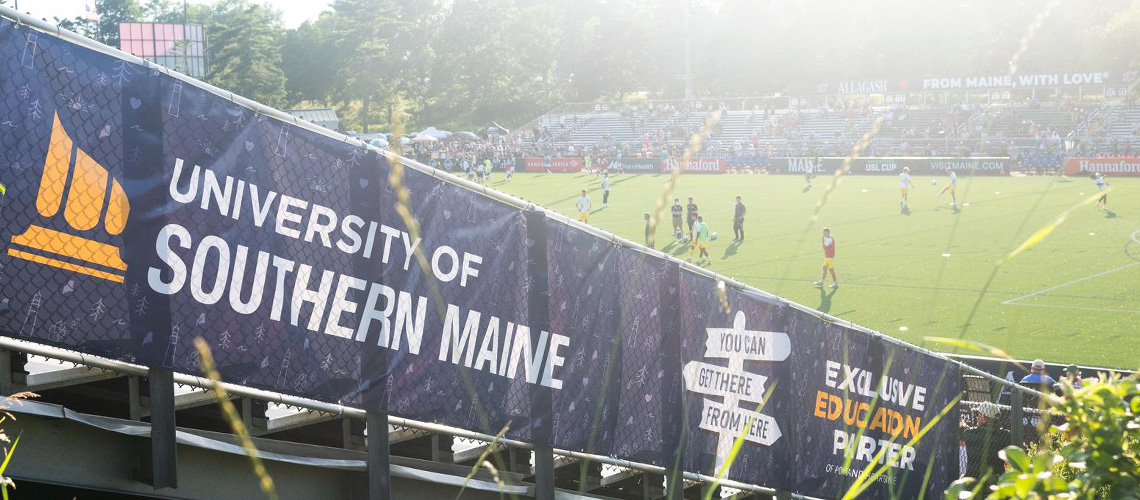 A banner with the USM logo and the words "exclusive education partner" is mounted on a fence at Fitzy Stadium.