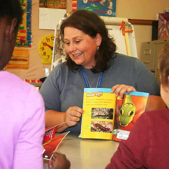 Elementary school teacher shows pages of a picture book to students.