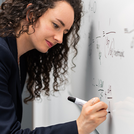 A student writing a mathematical formula on a whiteboard