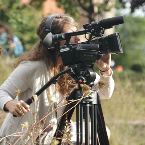 A student adjusting a camera on the campus green