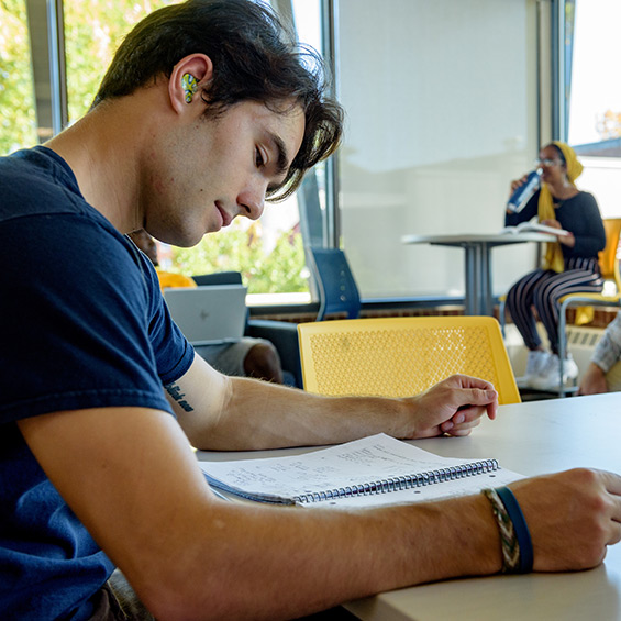 A student sits at a table and reads a notebook.