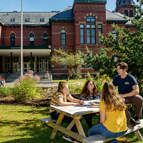 Students sitting at a picnic table in front of Corthell Hall.