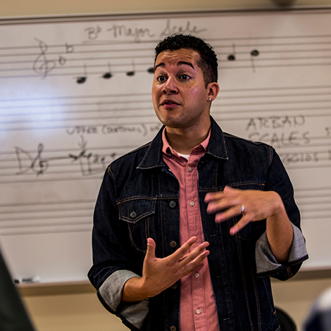 An instructor stands before a whiteboard with musical notes on it.