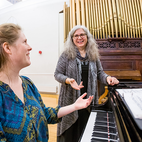 A piano instructor stands next to a student and in front of an organ.