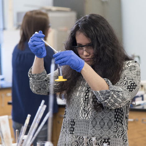 A student wearing blue gloves measures out liquid during an experiement.