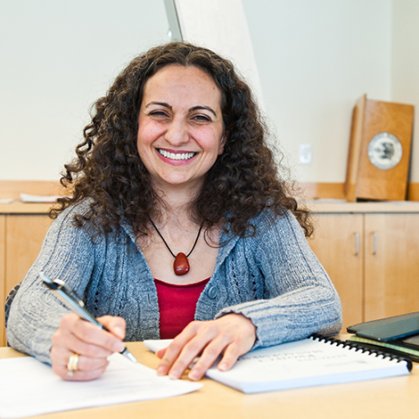 A student smiling while working in a notebook at a desk.