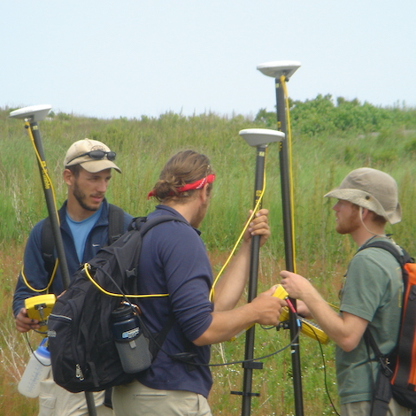 Three students set up equipment in a grassy field.
