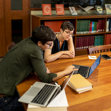 Two students study in the library with their books and computers.