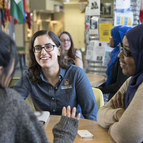 A group of diverse students sit around a table and talk.