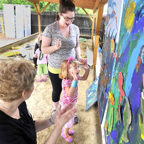 An art student from USM helps guide a child in painting a wall with bright colors.