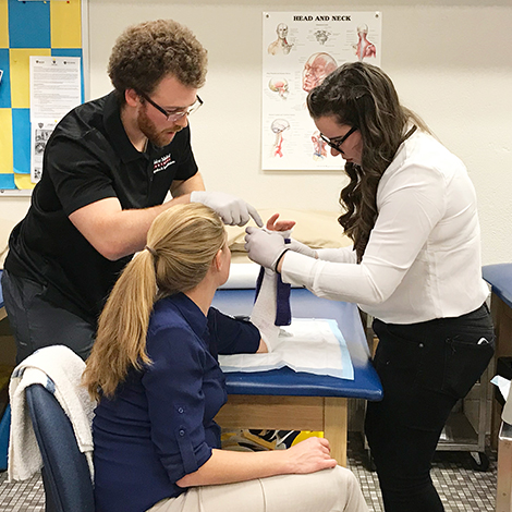 Athletic Training students work with a faculty member to practice wrapping an arm.