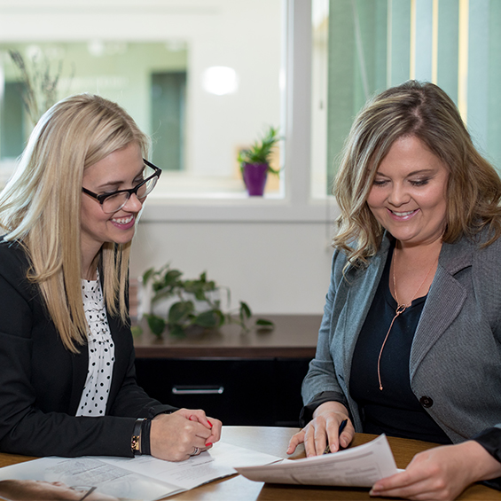 Two women sit at a table and review paperwork together.