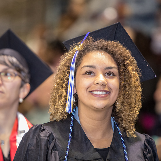 A student in a graduation cap and gown gazes upward.