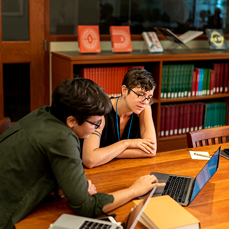 Two students studying with laptops at a table in the library.