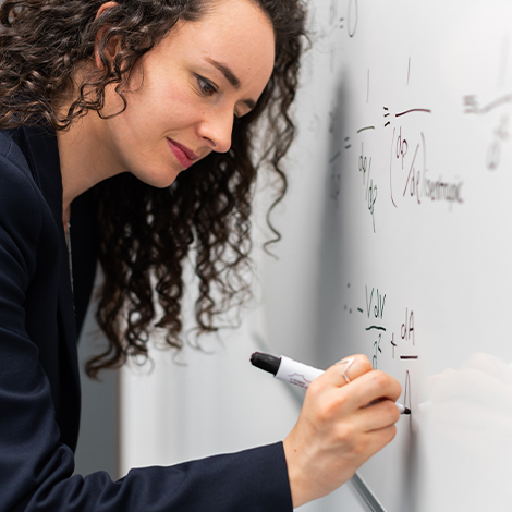 A woman writes a math equation on a whiteboard.