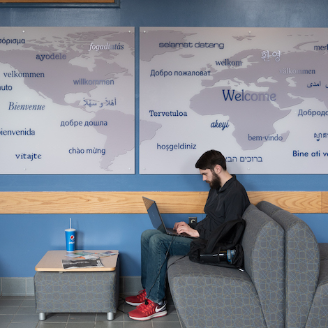 A student works on a laptop in front of a map of the world.