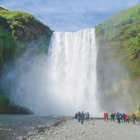 A group of USM tourism students stand near the base of a waterfall in Iceland.