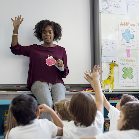 A teacher stands in front of a group of sitting students and goes through a lesson.