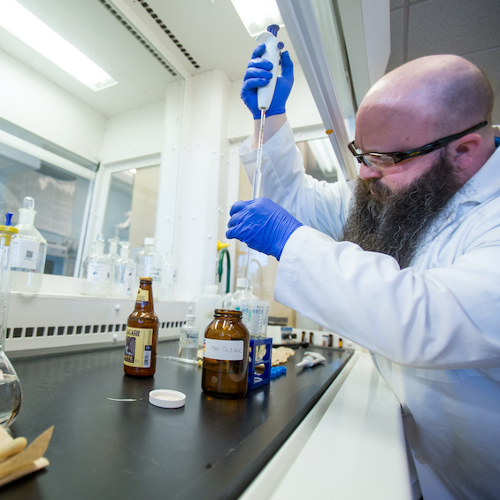 A long-bearded student wearing safety goggles transfers liquid into a set of test tubes in one of our chemistry labs.