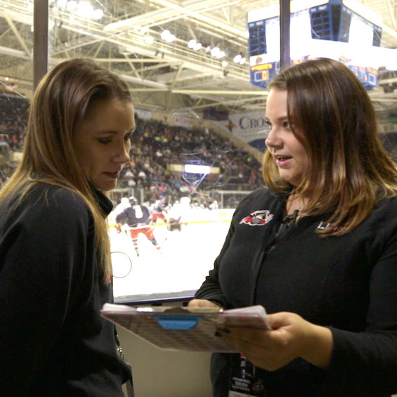 A sports management intern works for a hockey team during the internship and talks with someone during a hockey game.