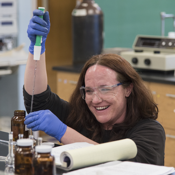 A student wearing safety goggles injects a liquid into a bottle.