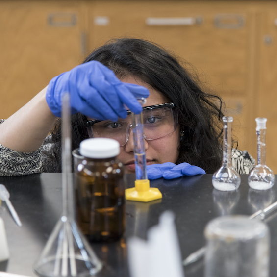 A student wearing safety glasses and gloves inserts liquid in a test tube.