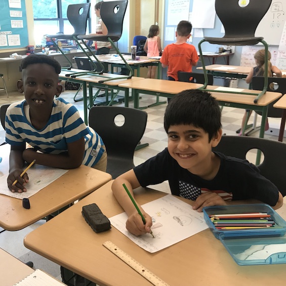 Two elementary school students smile in a classroom.