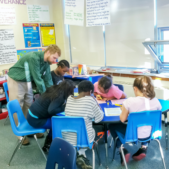 A teacher works with a group of young students in a classroom.