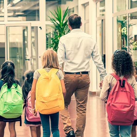 A teacher walks with a group of school children through a hallway.