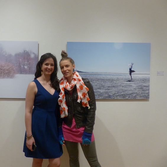 Two students pose in front of art pieces during a student exhibition.