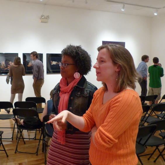 Two patrons stand together and discuss a piece of art they're looking at.