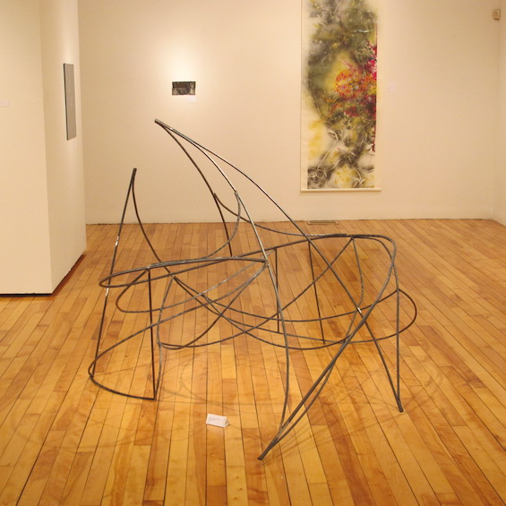 A metal, wire sculpture stands in the middle of the room in an art museum.