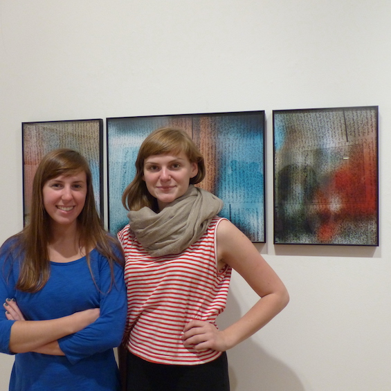 Two students pose in front of a series of art pieces.