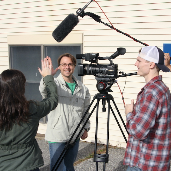 A group of students operates camera and sound equipment fo film student actors outdoors.