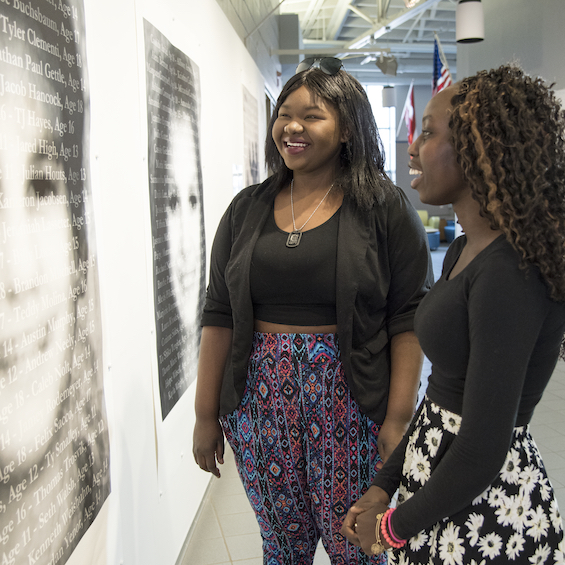 Two young women observe a large artwork hanging on the wall in a museum.