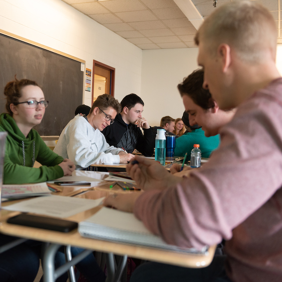 A group of students face each other and work on their assignments in class.