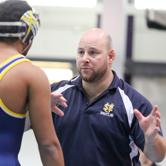 A coach describes a strategy to a wrestler using hand gestures.