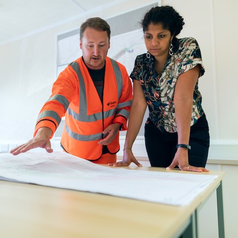 A man in bright orange construction safety wear talks about a map with a working professional.