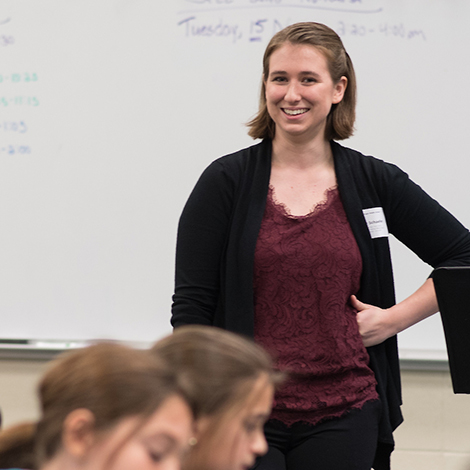 A student teacher smiles at a group of K-12 students in the classroom.