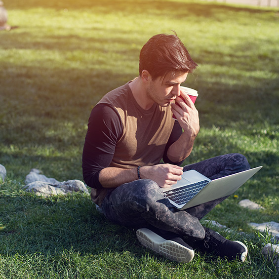 A student uses their laptop outside sitting on the grass.
