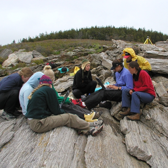 A group of students sit on a rocky area and conduct fieldwork.
