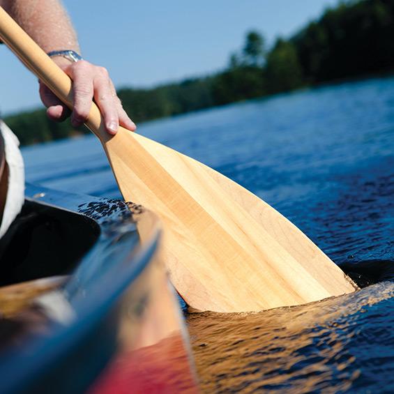 A hand holds an oar in the water on the side of a canoe.