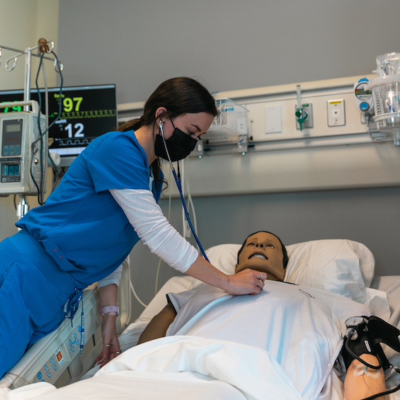 A nursing student practices using her stethoscope with a simulation mannequin.