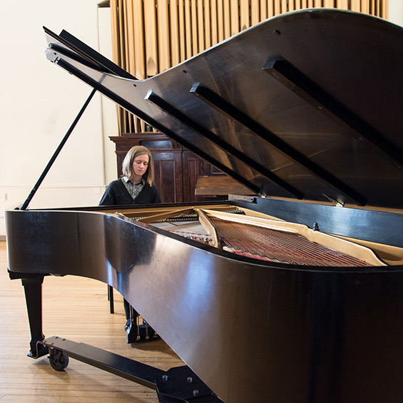 A student plays a grand piano in Corthell Hall.