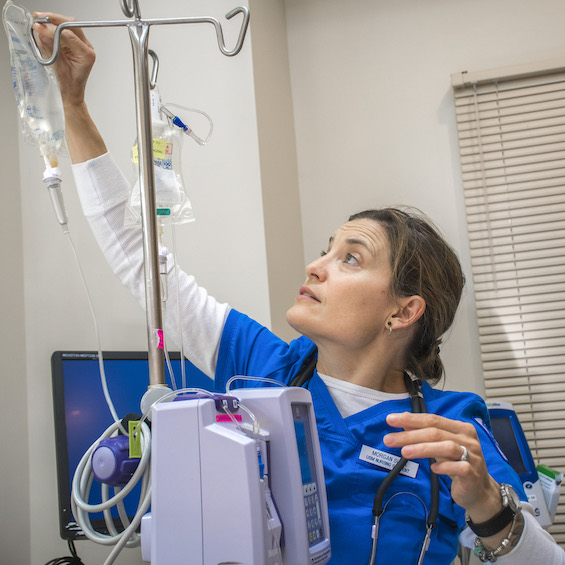 A nurse in blue scrubs adjusts an IV bag.
